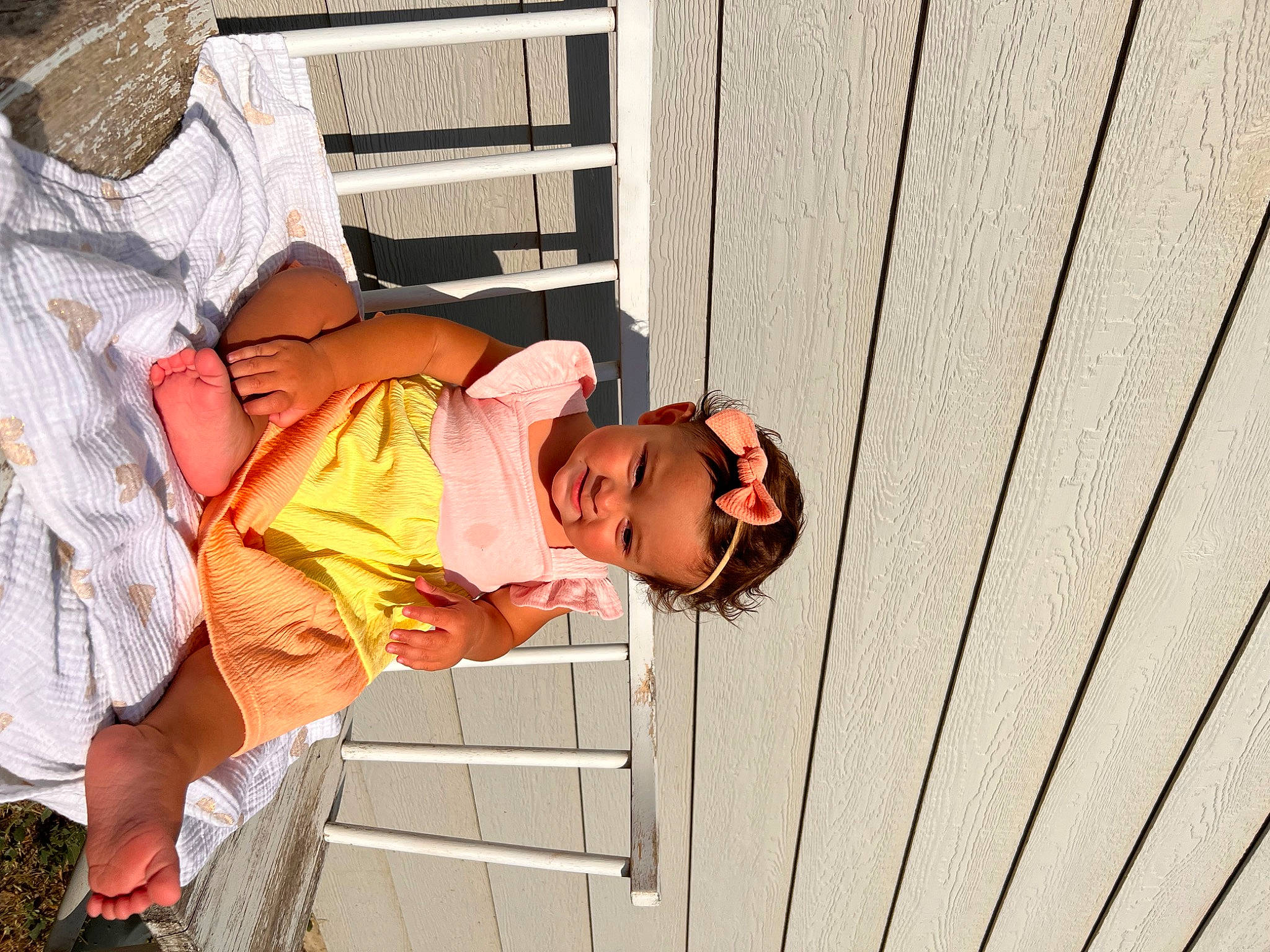 Sanya is registered to the contest to win money with this photo: child, eyewear, fence, flip_flops, fun, happy, hat, headwear, joy, leisure, person, sandal, shorts, siding, sitting, t_shirt, toddler, vacation, wood