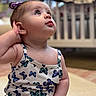 Hayden joined the competition — help win amazing prizes! baby, child, infant, girl, sitting, indoors, curious, looking_up, butterfly_pattern, clothing, hair_tie, hand, face, skin, crib, blurred_background, portrait, cute, young, expression