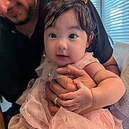 Elise joined the competition — help win amazing prizes! baby, child, adult, person, pigtails, pink_dress, golden_accents, holding, hand, face, eyes, smile, indoor, window_blinds, natural_light, curly_hair, cute, soft_fabric, toddler, family