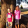 backpack, boots, boy, building, casual_clothing, child, daytime, expression, girl, grass, nature, outdoor, park, pink_shirt, shadow, shorts, sidewalk, standing, sunlight, tree