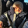 baby, child, car_seat, pacifier, blue_eyes, beanie, jacket, seatbelt, sunlight, indoors, portrait, winter_clothing, cute, infant, close_up, face, young_child, warm_clothing, dinosaur_patch, car_interior