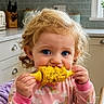 Pynelopi joined the competition — help win amazing prizes! child, toddler, corn, food, kitchen, curly_hair, blue_eyes, pink_clothing, rainbow_pattern, eating, hand, face, window, plant, drawer, countertop, cutlery_holder, scissors, appliance, natural_light