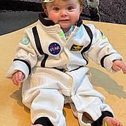 Isabella joined the competition — help win amazing prizes! astronaut_costume, baby, barefoot, bow_headband, child, costume, cute, eyes, face, feet, floor, hands, indoor, infant, playful, portrait, sitting, smiling, white_suit, wooden_surface