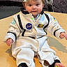 astronaut_costume, baby, barefoot, bow_headband, child, costume, cute, eyes, face, feet, floor, hands, indoor, infant, playful, portrait, sitting, smiling, white_suit, wooden_surface