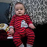 Draco is registered to the contest to win money with this photo: baby, infant, child, portrait, sitting, couch, pillow, leopard_print, red_clothing, striped_clothing, penguin_design, romper, wide_eyed, indoor, home, furniture, toys, feet, short_hair, face