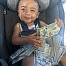 baby, car_seat, cash, child, currency, dollar_bills, happy, indoor, infant, looking_at_camera, money, personal_finance, photograph, portrait, seatbelt, sitting, smiling, toddler, travel, vehicle