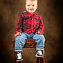 brown_background, casual_clothing, checkered_shirt, child, cute, fashion, footwear, happy, indoor, jeans, portrait, puma, red_shirt, sitting, smile, sneakers, studio_portrait, toddler, wooden_stool, young_child