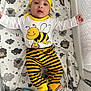 baby, infant, crib, bedding, bee_costume, hat, striped_pants, cute, child, lying_down, patterned_blanket, smiling, face, hands, feet, yellow, black, mesh_side, elephant_pillow, indoor