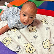 Liam joined the competition — help win amazing prizes! baby, infant, blanket, cartoon, play_mat, floor, child, face, eyes, clothing, striped_shirt, sock, indoor, colorful, toy_storage, expression, cute, young, soft, resting