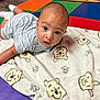baby, infant, blanket, cartoon, play_mat, floor, child, face, eyes, clothing, striped_shirt, sock, indoor, colorful, toy_storage, expression, cute, young, soft, resting