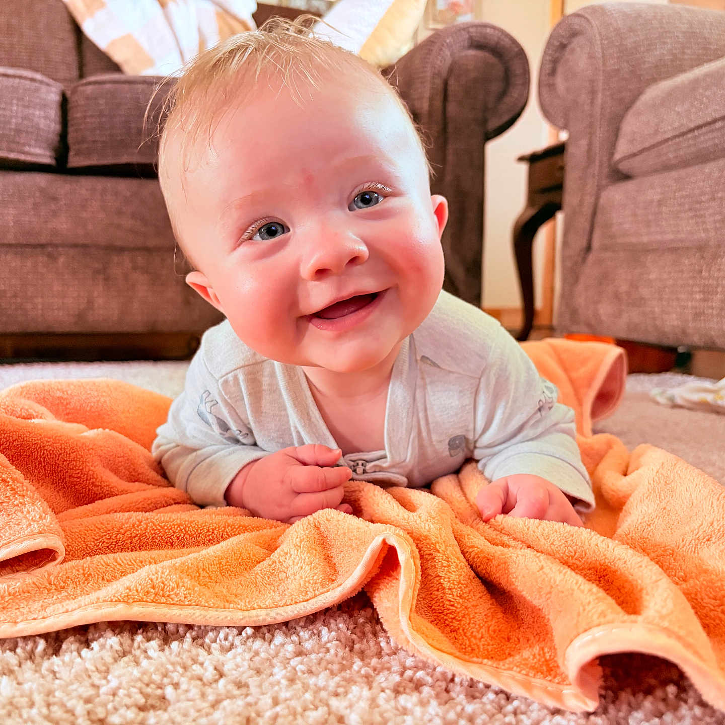 Derek is registered to the contest to win money with this photo: baby, blanket, carpet, child, clothing, couch, cute, face, floor, happy, home, indoors, infant, living_room, orange, person, propped_up, smiling, towel, young