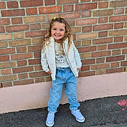 Melina a rejoint le concours — aidez-le/la à gagner de superbes lots ! blue_jeans, brick_wall, casual_clothing, child, curly_hair, daylight, fashion, girl, graphic_tee, happy, outdoor, portrait, posing, sidewalk, smiling, standing, urban, white_jacket, white_sneakers, yellow_hair_clips