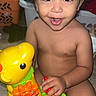 toddler, child, toy, yellow_toy, giraffe_toy, smiling, curly_hair, indoor, play, happy, person, skin, face, hand, furniture, floor, colorful, baby, cute, expression