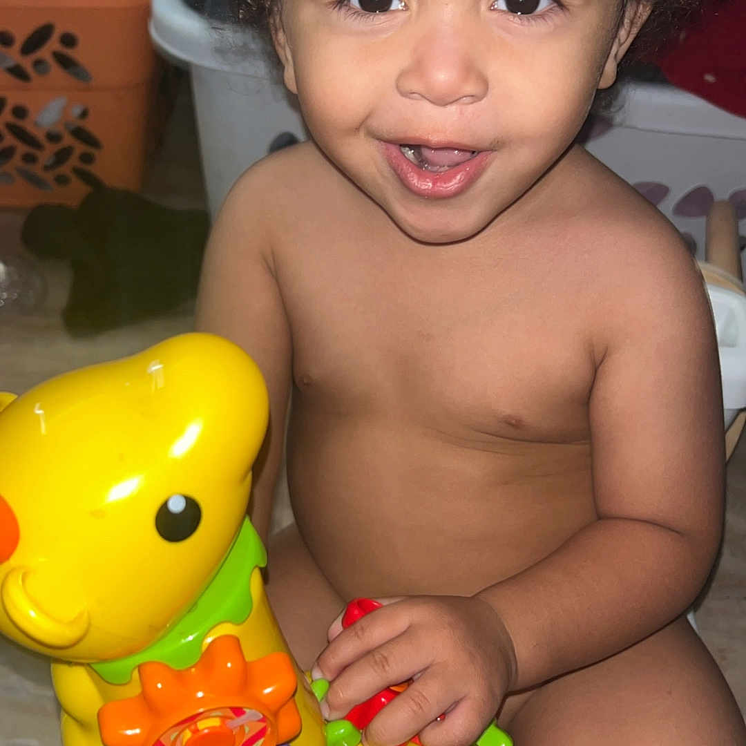 Zayden joined the competition — help win amazing prizes! toddler, child, toy, yellow_toy, giraffe_toy, smiling, curly_hair, indoor, play, happy, person, skin, face, hand, furniture, floor, colorful, baby, cute, expression