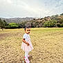 toddler, child, girl, pink_dress, white_tshirt, white_leggings, pink_shoes, grass, field, hill, trees, hollywood_sign, outdoor, sky, cloudy, standing, serious_expression, nature, daytime, park