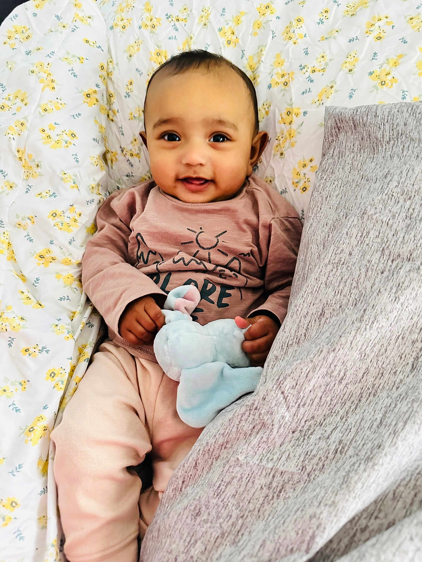 Madina is registered to the contest to win money with this photo: baby, infant, smiling, toy, plush_toy, elephant, blanket, floral_pattern, pillow, cozy_clothing, pink_clothes, lying_down, cute, child, happy, indoor, portrait, face, hands, cute_baby
