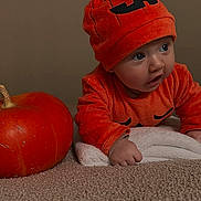 Zély a rejoint le concours — aidez-le/la à gagner de superbes lots ! baby, child, pumpkin, orange_clothing, hat, carpet, towel, indoor, cute, costume, face, hands, curious, holiday, autumn, seasonal, portrait, expression, crawling, soft_texture