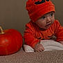 baby, child, pumpkin, orange_clothing, hat, carpet, towel, indoor, cute, costume, face, hands, curious, holiday, autumn, seasonal, portrait, expression, crawling, soft_texture