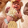 Alani is registered to the contest to win money with this photo: baby, infant, tutu, flower_headband, lace, pearl_necklace, tag, bed, blanket, soft_fabric, pink, cute, smile, portrait, newborn, person, lying_down, skin, hand, closeup