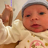 Alani is registered to the contest to win money with this photo: baby, infant, face, headwear, beanie, clothing, white_outfit, pattern, heart, stars, person, skin, foot, legs, indoors, string_lights, background, closeup, curious, lap