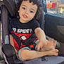 child, toddler, car_seat, curly_hair, black_shirt, spiderman, waving_hand, car_interior, seatbelt, window, daylight, cute, smiling, barefoot, shorts, seat, kid, young_child, casual_clothing, happy