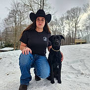 Bella joined the competition — help win amazing prizes! animal, black_dog, black_tshirt, cold_weather, collar, cowboy_hat, dog, footwear, house, jeans, kneeling, nature, outdoor, person, pet, serious_expression, sky, snow, trees, winter