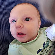 Kylan is registered to the contest to win money with this photo: baby, infant, face, eyes, mouth, clothing, green_shirt, pattern, fish_design, texture, blue_background, closeup, portrait, child, newborn, skin, expression, looking_up, cute, young