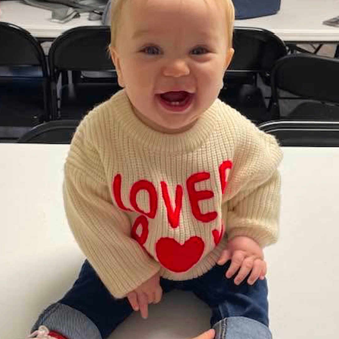 Jaxon Williams is registered to the contest to win money with this photo: baby, babylaughing, bodypart, clothing, face, finger, footwear, furniture, happy, head, knitwear, pants, person, photography, portrait, shoe, sitting, sneaker, sweater, table