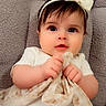 baby, infant, child, portrait, close_up, wide_eyes, headband, bow, dress, white_clothing, sitting, lying_down, indoors, blanket, couch, textile, hands, fashion, adorable, photography