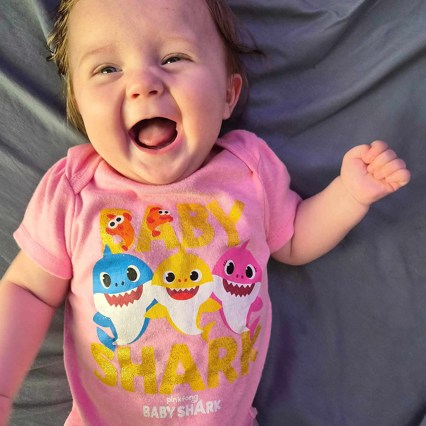 Charlotte joined the competition — help win amazing prizes! baby, child, infant, smiling, happy, onesie, pink_clothing, baby_shark, lying_down, blanket, cute, face, hand, expression, human, portrait, cheerful, young_child, indoors, clothing