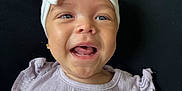 Eira is registered to the contest to win money with this photo: baby, child, smiling, headband, bow, clothing, purple_shirt, face, happy, portrait, infant, cute, person, young_child, skin, eyes, mouth, sleeves, black_background, closeup