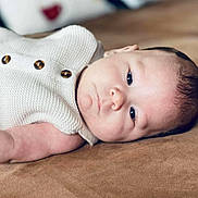 Thélio a rejoint le concours — aidez-le/la à gagner de superbes lots ! arm, baby, brown_background, buttons, calm, child, closeup, cute, eyes, face, indoor, infant, knitted_clothing, lying_down, newborn, person, portrait, skin, sleepy, soft_surface