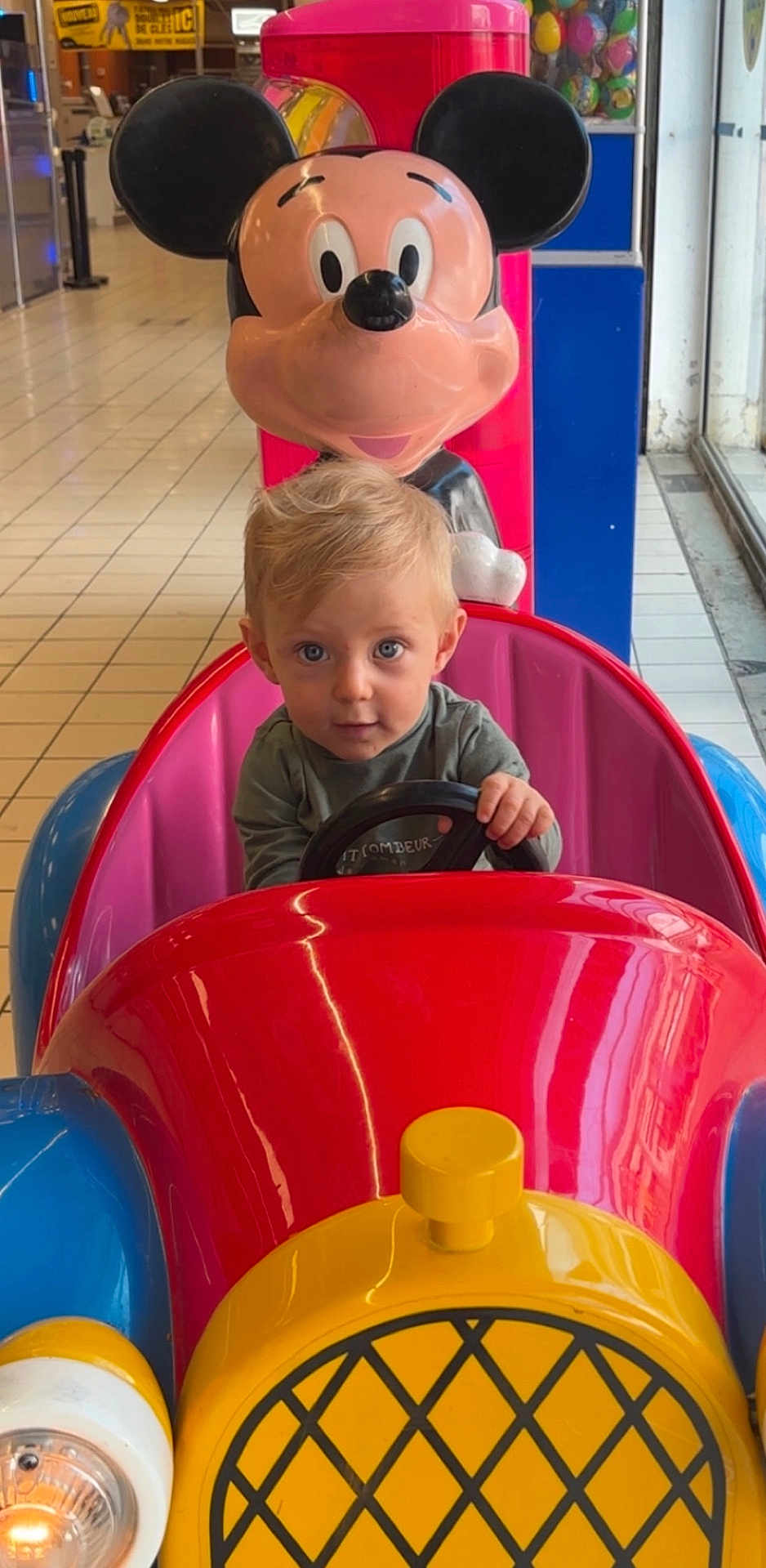 Ezio participe au concours pour gagner de l'argent avec cette photo : toddler, child, mickey_mouse, arcade, kiddie_ride, colorful, toy_car, steering_wheel, indoor, mall, floor_tiles, blond_hair, blue_eyes, plastic, amusement, playful, cute, portrait, entertainment, fun