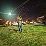 child, grass, night, fireworks, car, streetlight, running, blur, suburban, celebration, joy, outdoor, dark_sky, motion, person, casual_clothing, building, lawn, event, fun
