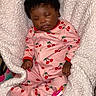baby, infant, sleeping, portrait, pink_outfit, cherry_pattern, onesie, blanket, white_blanket, pacifier, curly_hair, dark_skin, closed_eyes, peaceful, indoors, cozy, nursery, lying_down, child, photography