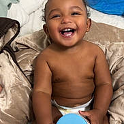Wyatt is registered to the contest to win money with this photo: baby, smiling, diaper, blanket, bed, container, blue_lid, happy, child, indoors, skin, hand, sitting, cute, toddler, plush, head, face, room, comfort