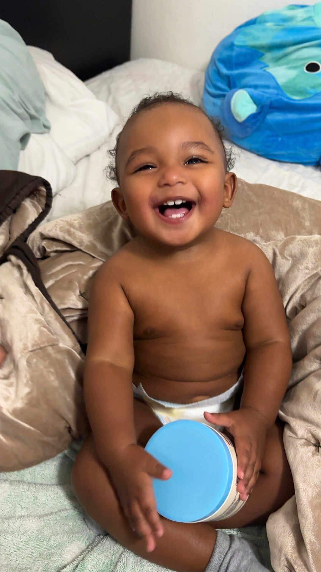 Wyatt is registered to the contest to win money with this photo: baby, smiling, diaper, blanket, bed, container, blue_lid, happy, child, indoors, skin, hand, sitting, cute, toddler, plush, head, face, room, comfort