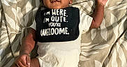 Khylo joined the competition — help win amazing prizes! baby, infant, onesie, bib, bed, blanket, striped_socks, smiling, happy, lying_down, child, cute, indoors, person, text_on_bib, patterned_bedspread, skin, face, hand, foot