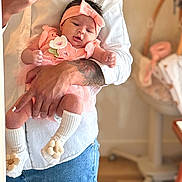 Hadassah is registered to the contest to win money with this photo: baby, infant, adult, holding, pink_outfit, headband, white_shirt, jeans, tattoo, indoor, nursery, blurred_background, sock, flower, cute, portrait, person, hand, skin, toddler
