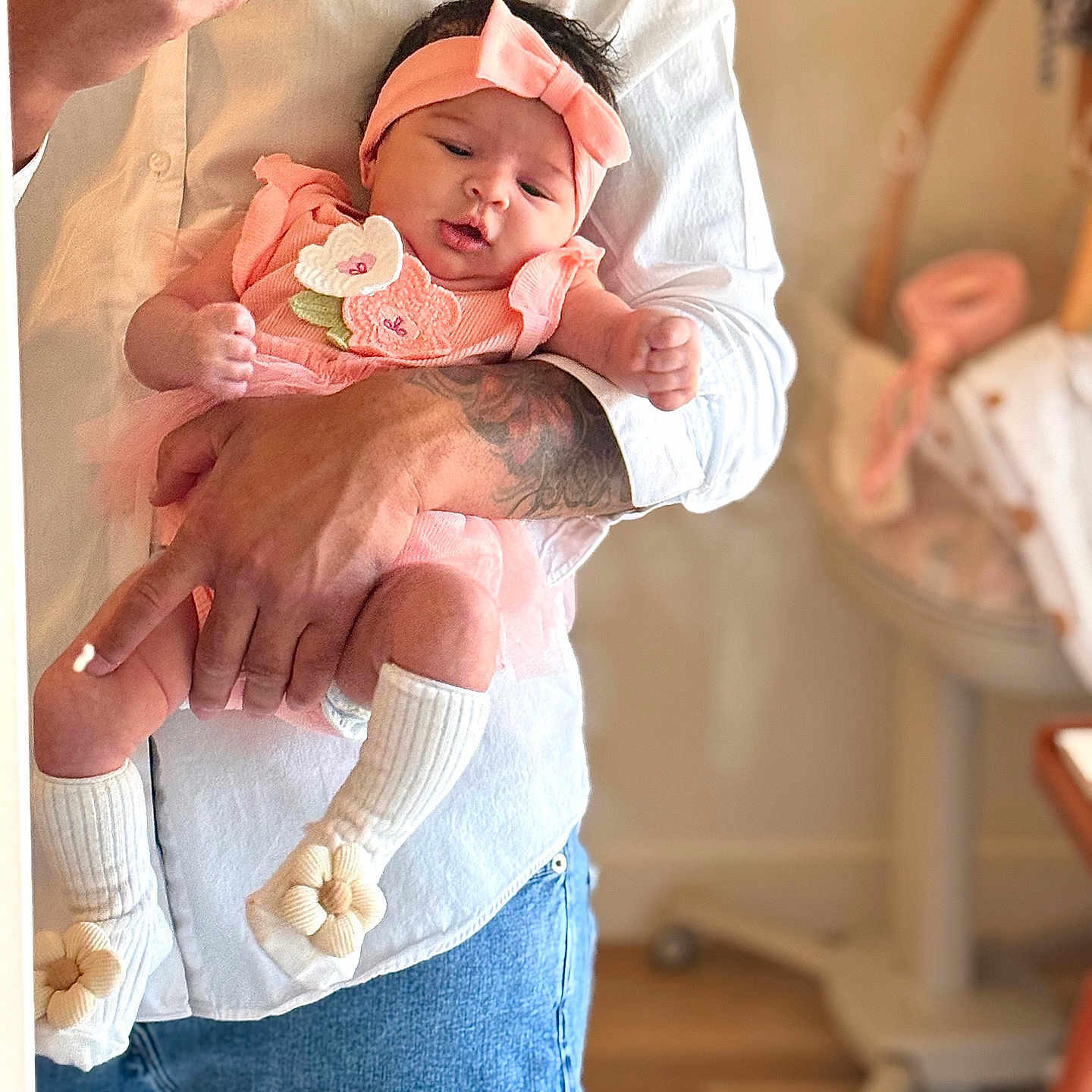 Hadassah is registered to the contest to win money with this photo: adult, baby, blurred_background, cute, flower, hand, headband, holding, indoor, infant, jeans, nursery, person, pink_outfit, portrait, skin, sock, tattoo, toddler, white_shirt