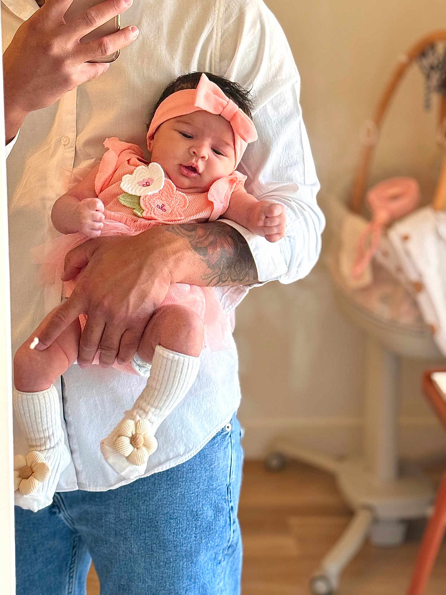 Hadassah is registered to the contest to win money with this photo: baby, infant, adult, holding, pink_outfit, headband, white_shirt, jeans, tattoo, indoor, nursery, blurred_background, sock, flower, cute, portrait, person, hand, skin, toddler