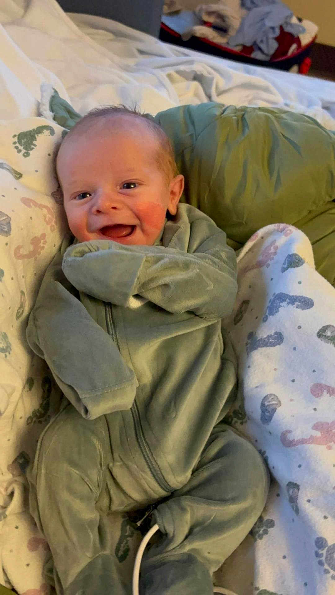 Jon is registered to the contest to win money with this photo: baby, smiling, infant, onesie, blanket, footprint_pattern, cozy, lying_down, happy, child, indoor, soft, cute, clothing, face, head, newborn, warm, expression, comfort