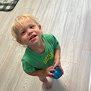 Jackson joined the competition — help win amazing prizes! child, toddler, blonde_hair, green_shirt, toy, blue_toy, barefoot, floor, wood_floor, indoor, smiling, looking_up, curious, home, welcome_mat, light, casual_clothing, happy, person, young_child