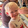 child, toddler, blonde_hair, smile, tank_top, red_truck, adult, glasses, indoor, wooden_structure, person, casual_clothing, curly_hair, happy, family, people, background, standing, childhood, daylight