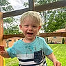 Jackson is registered to the contest to win money with this photo: child, toddler, outdoor, grass, trees, wooden_structure, smiling, happy, blonde_hair, striped_shirt, play, nature, daylight, casual_clothing, face, person, greenery, young_child, background, house