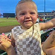 Asher is registered to the contest to win money with this photo: toddler, child, smiling, baseball, stadium, sports, checkered_shirt, sleeveless, hand_held, outdoor, evening, lights, face, person, spectator, seating, tattoo, nail_polish, happy, fun