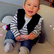 Lucie a rejoint le concours — aidez-le/la à gagner de superbes lots ! toddler, child, smiling, sitting, bottle, striped_clothing, vest, jeans, socks, couch, indoor, cozy, heart_effects, baby, happy, cute, portrait, furniture, home, casual