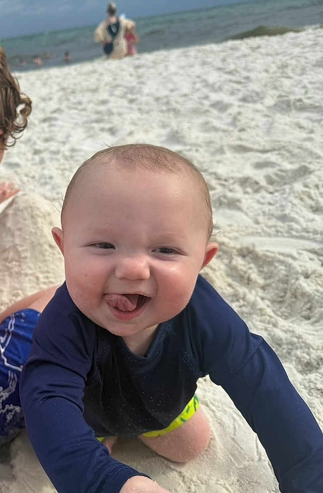 Wyatt is registered to the contest to win money with this photo: baby, child, beach, sand, ocean, water, play, smile, tongue, navy_shirt, shorts, sunny, outdoor, summer, fun, happy, cute, person, nature, vacation