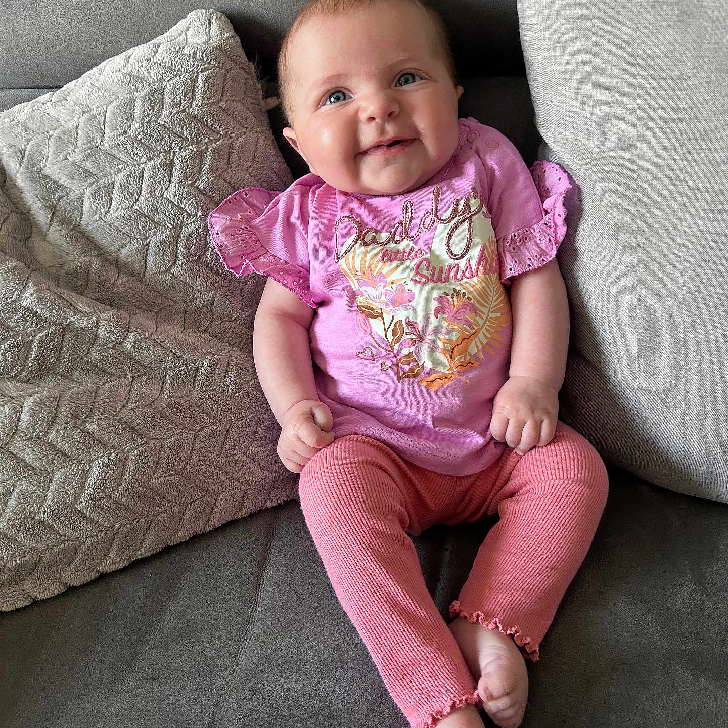 Dulcie is registered to the contest to win money with this photo: apparel, baby, child, comfortable, couch, cozy, cute, expression, face, happy, indoor, infant, person, pillows, pink_clothing, portrait, relaxing, sitting, smiling, young_child
