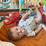 baby, pacifier, plush_toy, octopus, colorful_toys, play_mat, infant, white_onesie, activity_cube, soft_blanket, indoor, child, cute, toy_rings, crib_bars, floor, play_area, smiling, lying_down, curious
